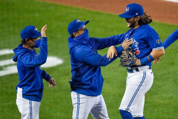 Blue Jays manager Charlie Montoyo, centre, and shortstop Bo Bichette, right, celebrate a win in September. Radio listeners will hear Sportsnet's TV feed of the game  (Adrian Kraus/The Associated Press - image credit)