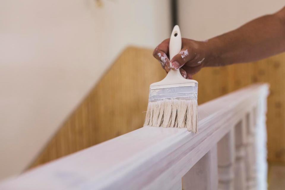 A close up of a paint brush being uses on a white railing. 