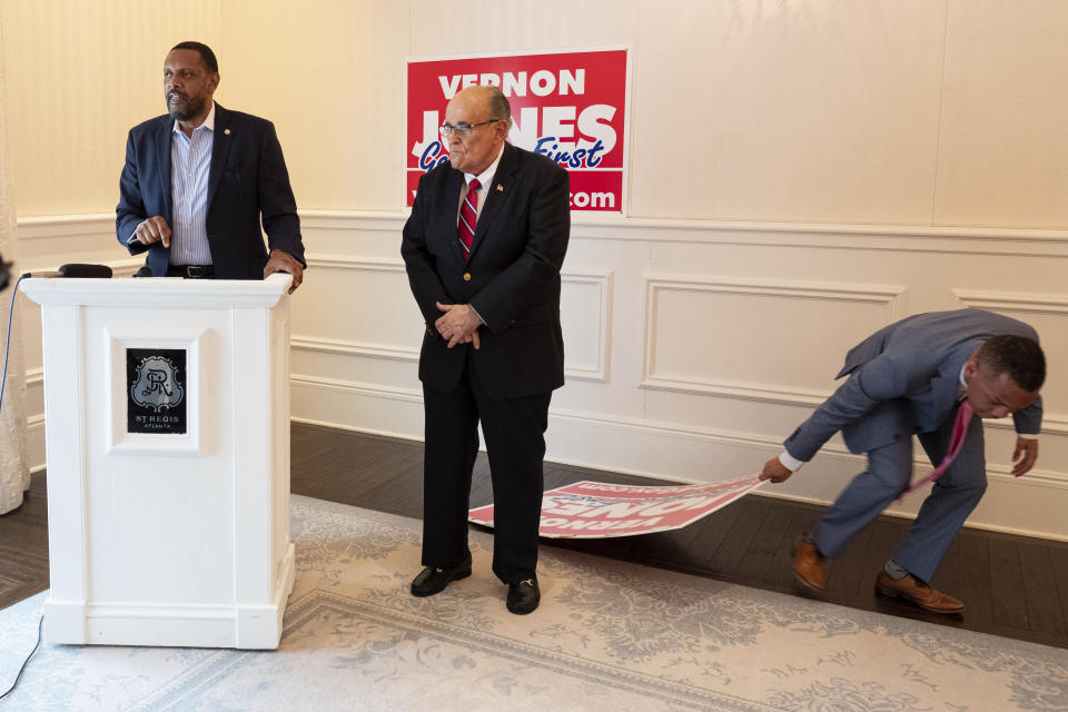 An aide drags away a fallen campaign sign while Vernon Jones speaks after Rudy Giuliani endorsed him for GOP candidate for Governor of Georgia during a press conference Wednesday afternoon, June 30, 2021 in Atlanta, Ga. (AP Photo/Ben Gray)