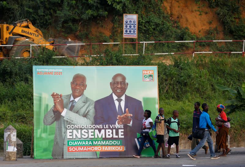 People walk pass next to a campaign bilboard showing the candidats of the ruling coalition party, the Rally of Houphouetists for Democracy and Peace (RHDP) ahead of the legislative election in Abidjan