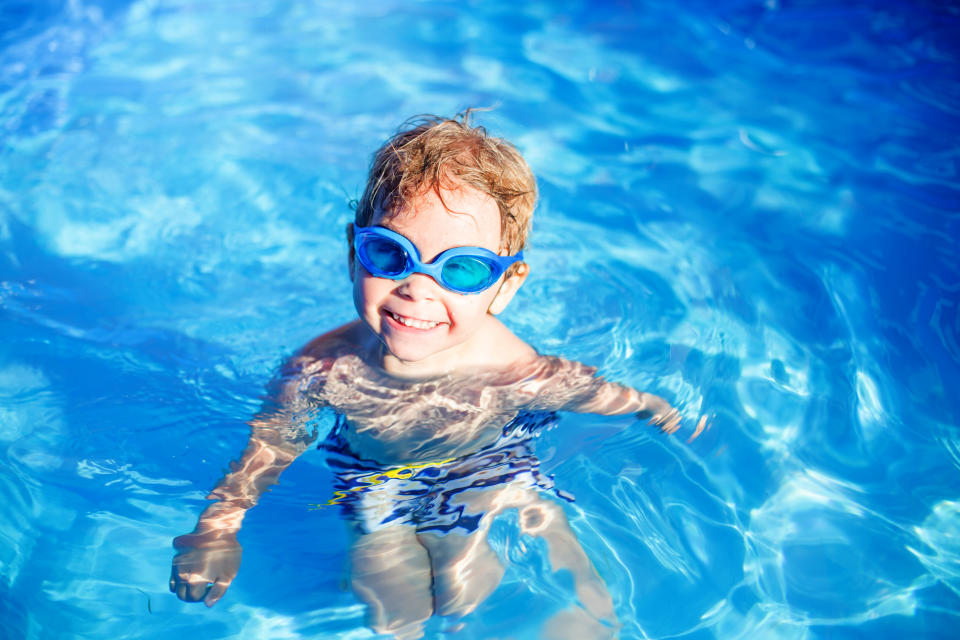 Beautiful toddler child, blond boy, swimming in a pool in backyard on sunset