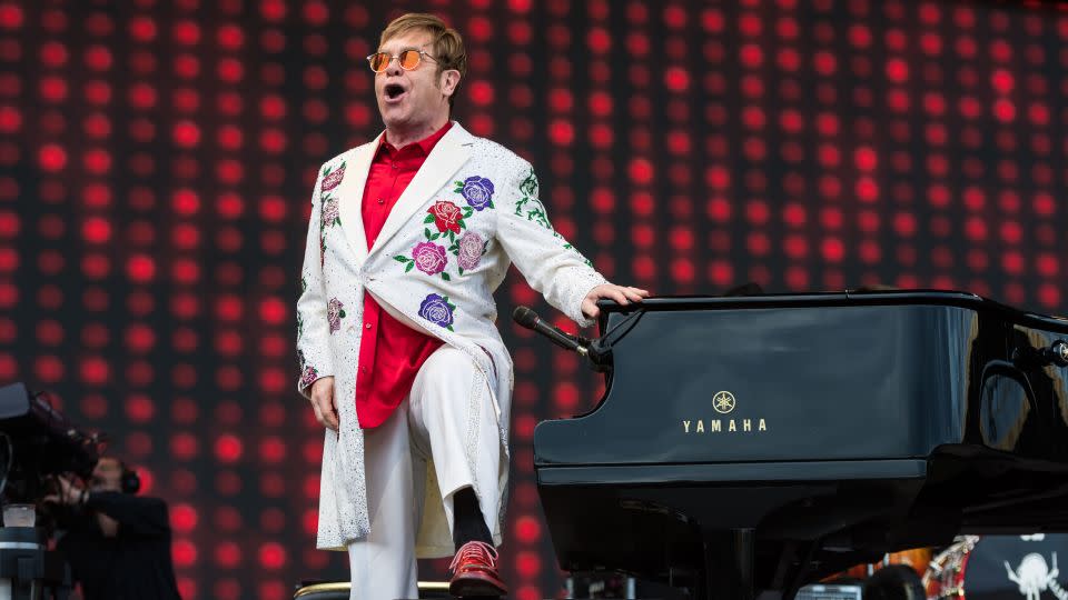 Elton John is never far from a piano — and never far from an extravagant outfit. - Ian Gavan/Getty Images