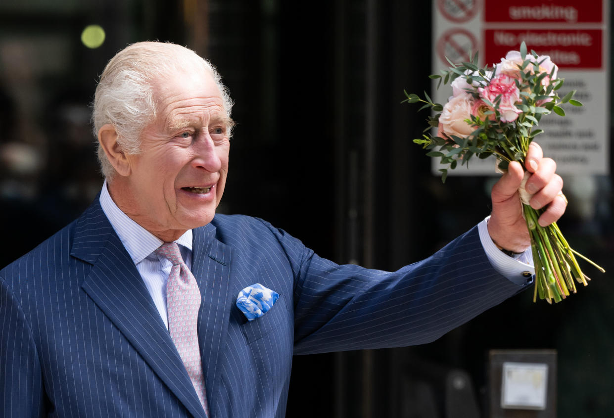 King Charles holds a bouquet in his left hand as he greets the public outside a London cancer center.