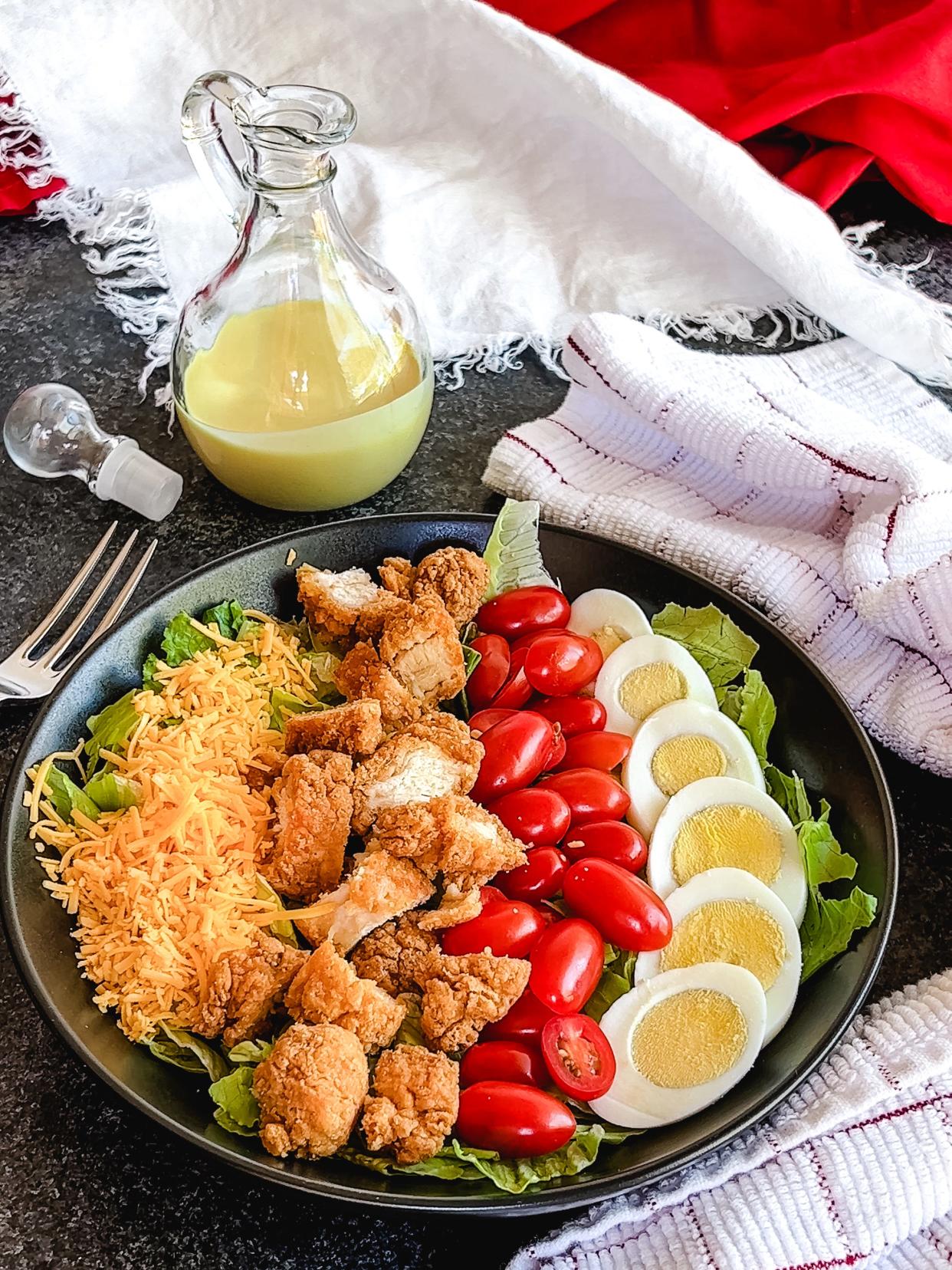 Southern Fried Chicken Salad is a symphony of flavors and textures featuring crisp lettuce, golden fried chicken strips, creamy hard-boiled eggs, tomatoes, and shredded cheese, all drizzled with a sweet and tangy dressing.