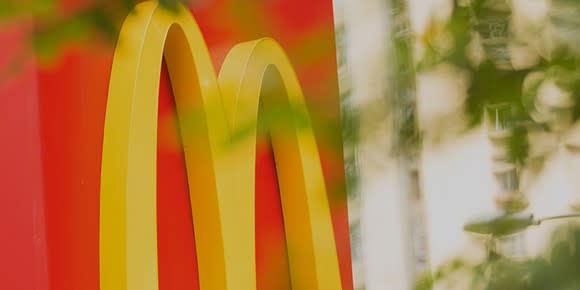 Detail of McDonald's red and yellow signage behind leafy, blurred foreground.