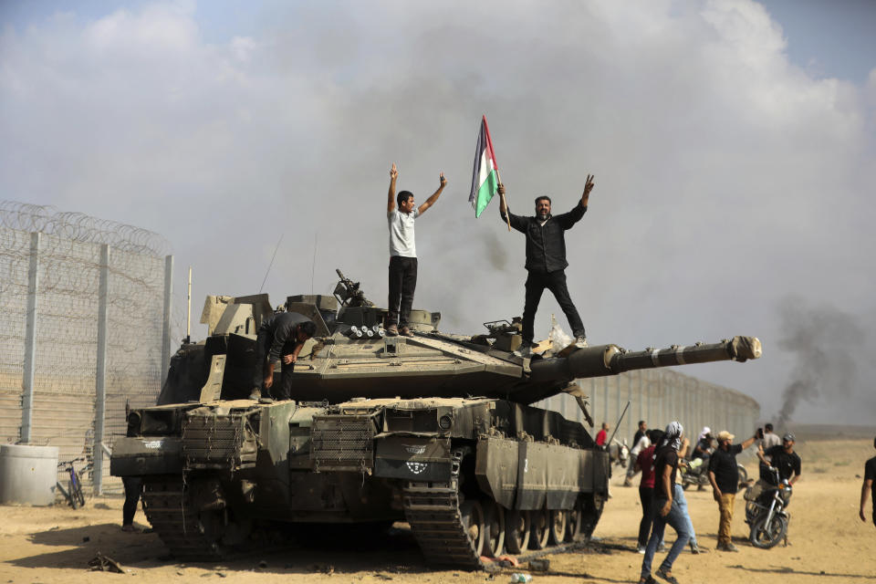 FILE - Palestinians wave their national flag and celebrate by a destroyed Israeli tank at the southern Gaza Strip fence east of Khan Younis on Saturday, Oct. 7, 2023. (AP Photo/Yousef Masoud, File)