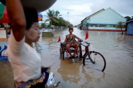 A man sits on his cart which he attached with National League for Democracy (NLD) party flags along a flooded street in Yangon in this September 30, 2015 file photo. REUTERS/Soe Zeya Tun/Files