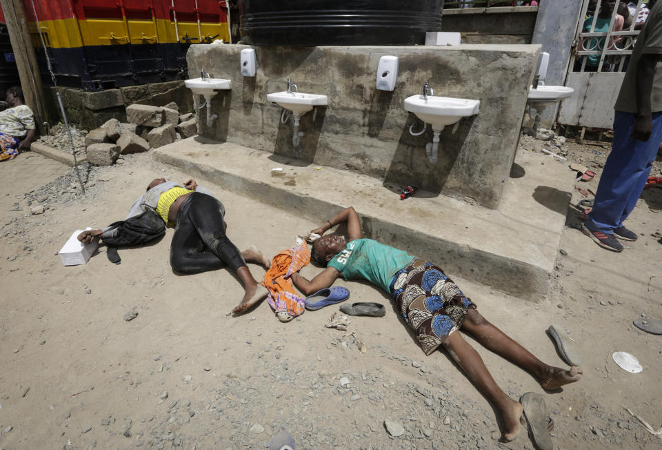 Two women who were injured after being trampled lay on the ground, after residents desperate for a planned distribution of food for those suffering under Kenya's coronavirus-related movement restrictions pushed through a gate and created a stampede, causing police to fire tear gas and leaving several injured, at a district office in the Kibera slum, or informal settlement, of Nairobi, Friday, April 10, 2020. (AP Photo/Khalil Senosi)