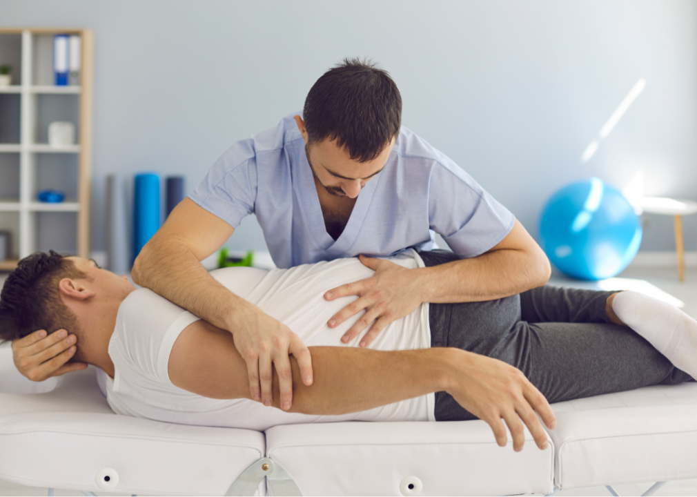 A chiropractor adjusts the back of a patient on his exam table.