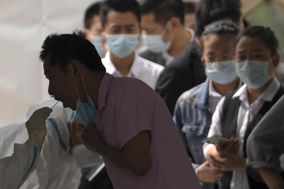 Workers line up to get a throat swab sample taken at a coronavirus test site set up near a commercial office complex, Sunday, April 24, 2022, in Beijing. Beijing is on alert after 10 middle school students tested positive for COVID-19, in what city officials said was an initial round of testing. (AP Photo/Andy Wong)
