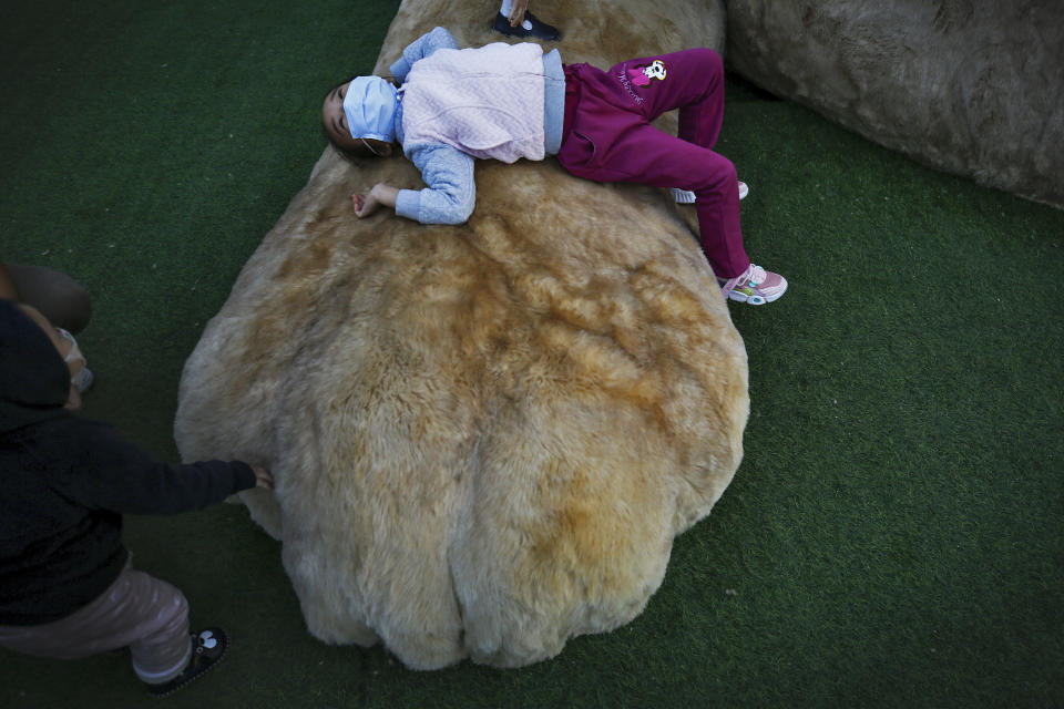 Children wearing face masks to help curb the spread of the coronavirus play on a paw of a giant cat structure on display at a commercial office building in Beijing, Sunday, Oct. 18, 2020. (AP Photo/Andy Wong)