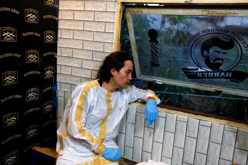 Herman Maulanasyah, a 40-year-old hair stylish, takes a rest after giving a haircut to a customer at his barbershop, while wearing a handmade protective suit in a tribute to the country's medical workers tackling the coronavirus disease (COVID-19) in Bogor