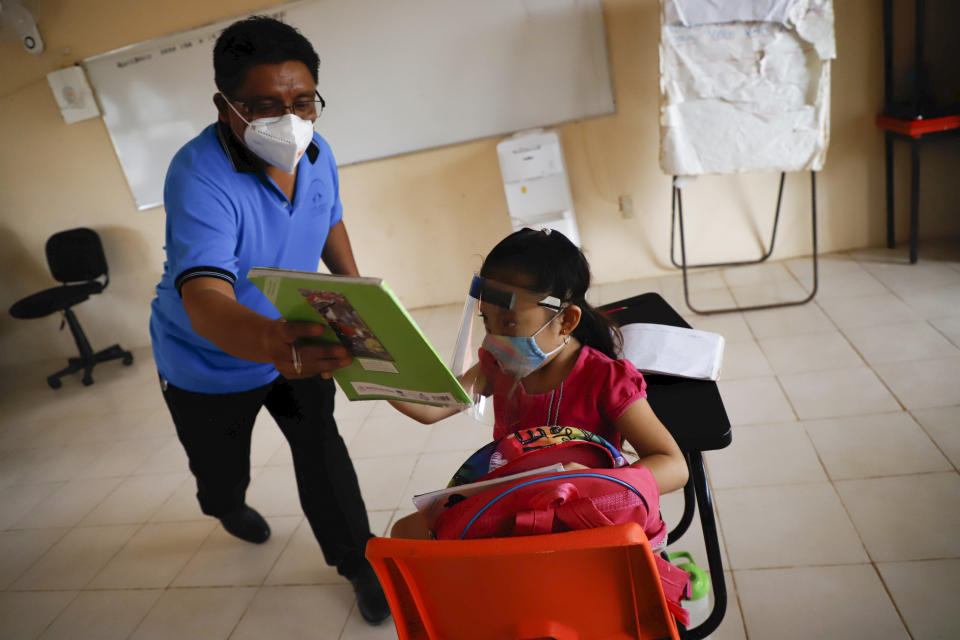 Wering a mask to curb the spread of the new coronavirus, a teacher hands a workbook to his 10-year-old student Jade Chan Puc during the first day of class at the Valentin Gomez Farias Indigenous Primary School in Montebello, Hecelchakan, Campeche state, Monday, April 19, 2021. Campeche is the first state to transition back to the classroom after a year of remote learning due to the pandemic. (AP Photo/Martin Zetina)