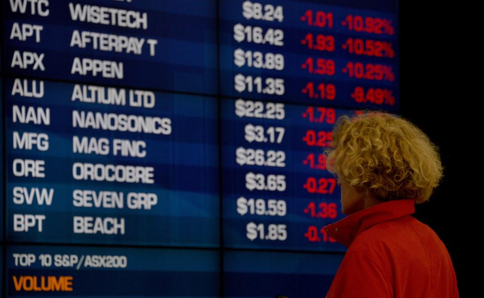 A woman ooks at share prices on a big screen. (Source: Getty)