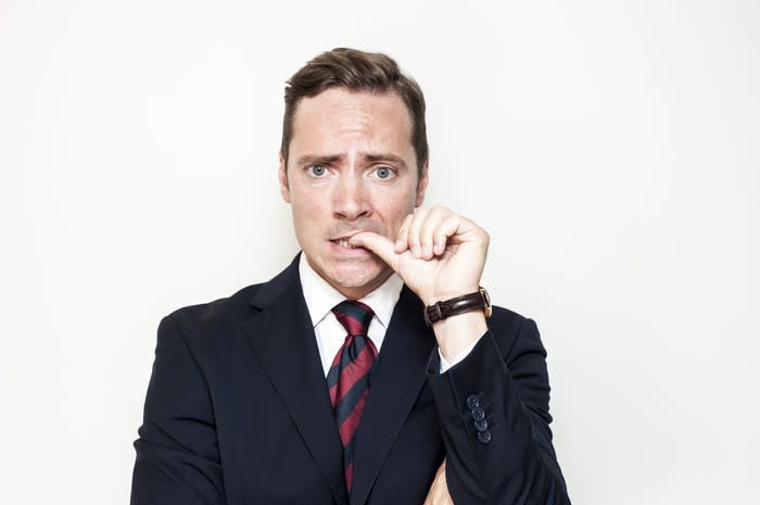 A man in a suit looking nervous, biting his thumbnail.