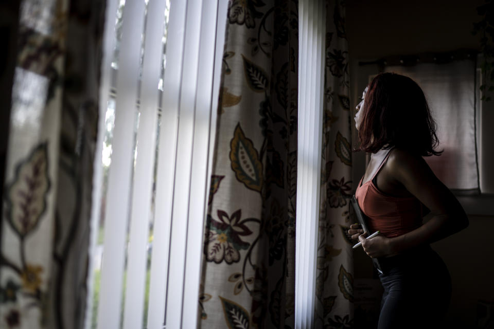 Victoria Gwynn, 21, looks out the window as a car she doesn't recognize pulls up outside her home in Louisville, Ky., Monday, Aug. 28, 2023. Since she was shot and injured in a park in 2021, Gwynn doesn't walk alone through her neighborhood and gets suspicious when cars slow past her house. (AP Photo/David Goldman)