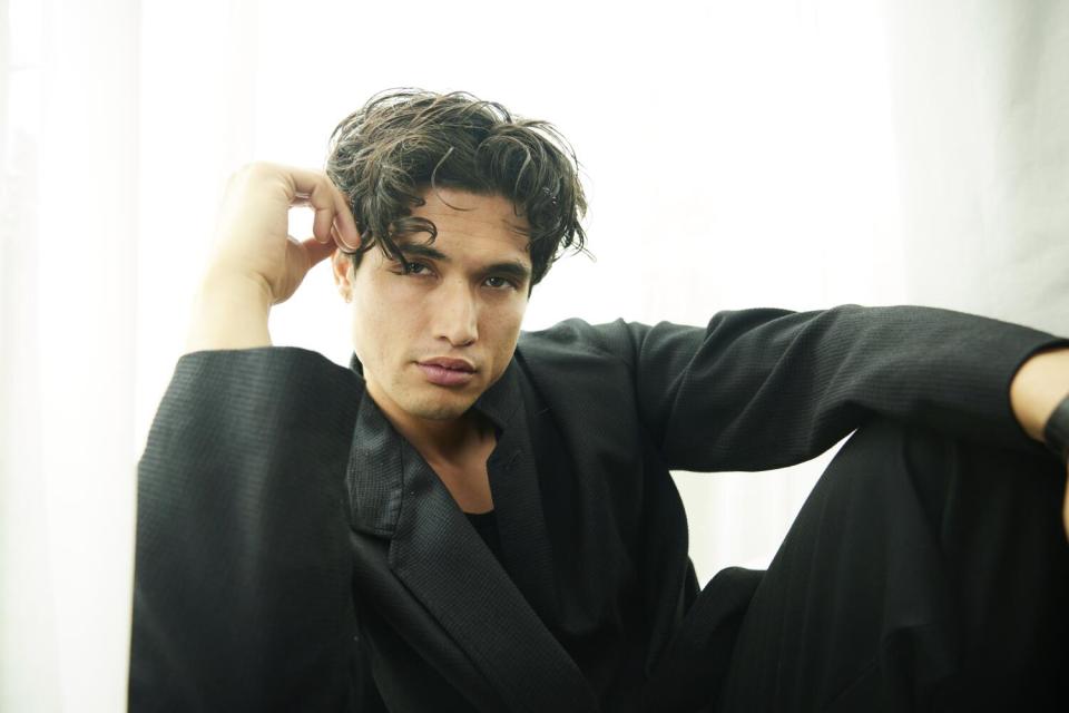 Charles Melton crouches on the floor for a portrait.