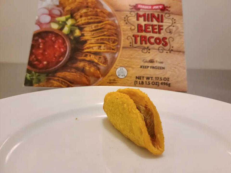 A taco with a beef filling on a plate with a brown box with pictures of tacos behind