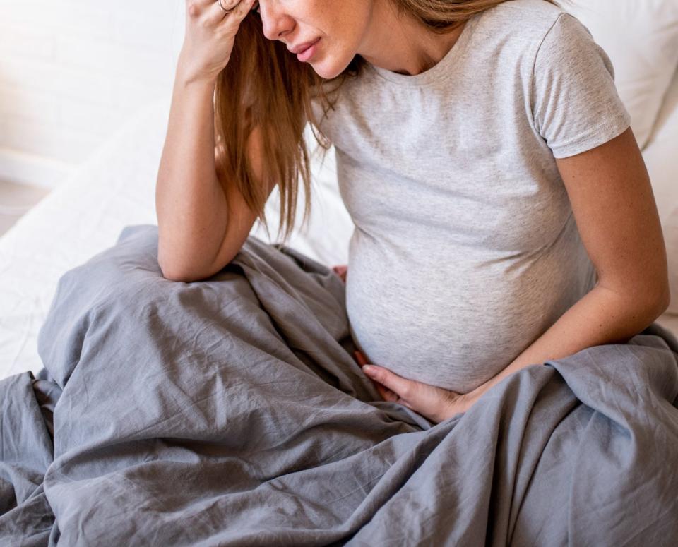 A pregnant woman grabs her forehead in an emotional state while she sits in bed