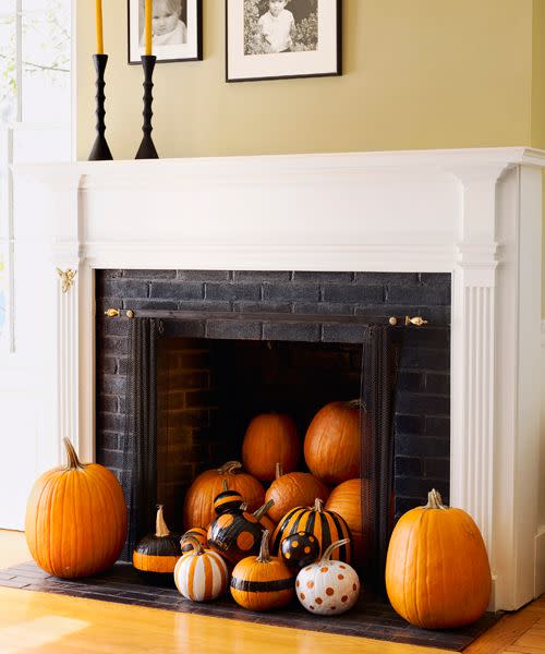 <p>Instead of the usual haunts, try grouping pumpkins in a less-expected locale, like an unused fireplace. For the these graphic gourds, use painter's tape and self-adhesive paper to mark off stripes and circles. Spray with glossy black and white paint, then casually pile in the hearth.</p>
