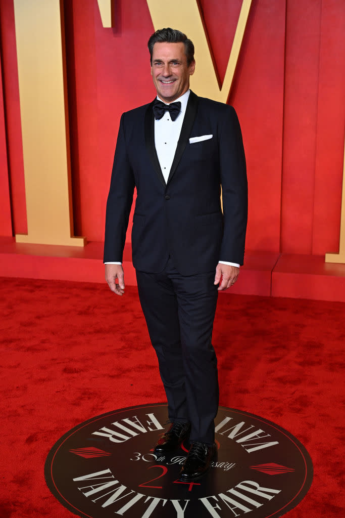 Man in a black tuxedo with a bow tie standing on a Vanity Fair event carpet