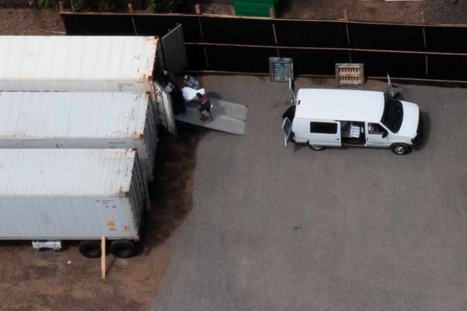 Workers move body bags into refrigerated storage containers adjacent to the Maui Police Forensic Facility where human remains are stored in the aftermath of the Maui wildfires in Wailuku, Hawaii on August 14, 2023.