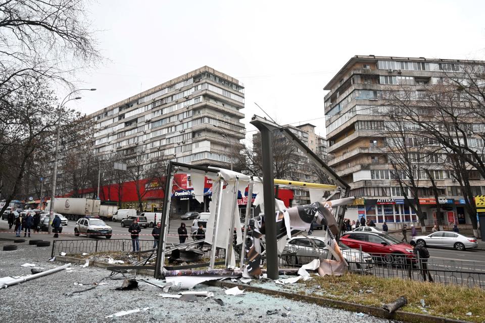 People near a cordoned-off area in Kyiv, showing a destroyed structure surrounded by broken glass.