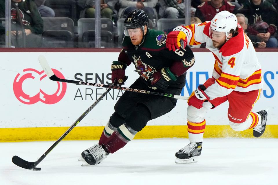 Arizona Coyotes left wing Lawson Crouse (67) shields the puck from Calgary Flames defenseman Rasmus Andersson in the first period during an NHL hockey game, Wednesday, Feb. 22, 2023, in Tempe, Ariz. (AP Photo/Rick Scuteri)