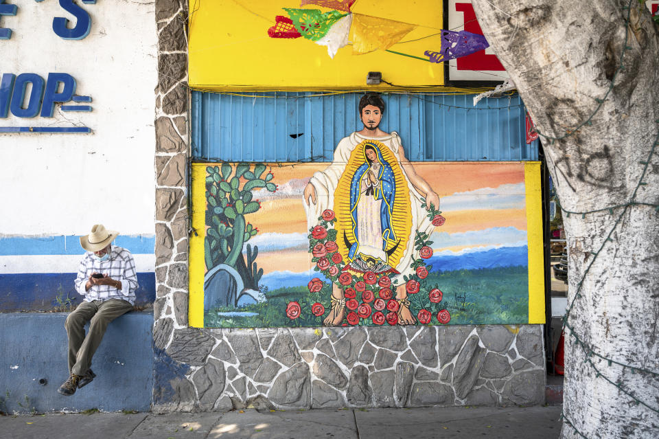 En esta fotografía tomada por Oscar Rodriguez Zapata, una persona revisa su teléfono celular cerca de un mural callejero de la Guadalupana en Los Ángeles, en julio de 2020. (Oscar Rodriguez Zapata vía AP)