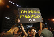 FILE - In this Nov. 7, 2019, file, photo, an anti-government protester holds up a placard in front the Lebanese electricity company headquarters, during ongoing protests against the Lebanese government and the corruption, in Beirut, Lebanon. Lebanon's energy minister said Thursday, July 16, 2020 the country's worsening economic crisis is making it increasingly difficult to attract investors for its ailing electricity sector. (AP Photo/Hussein Malla, File)