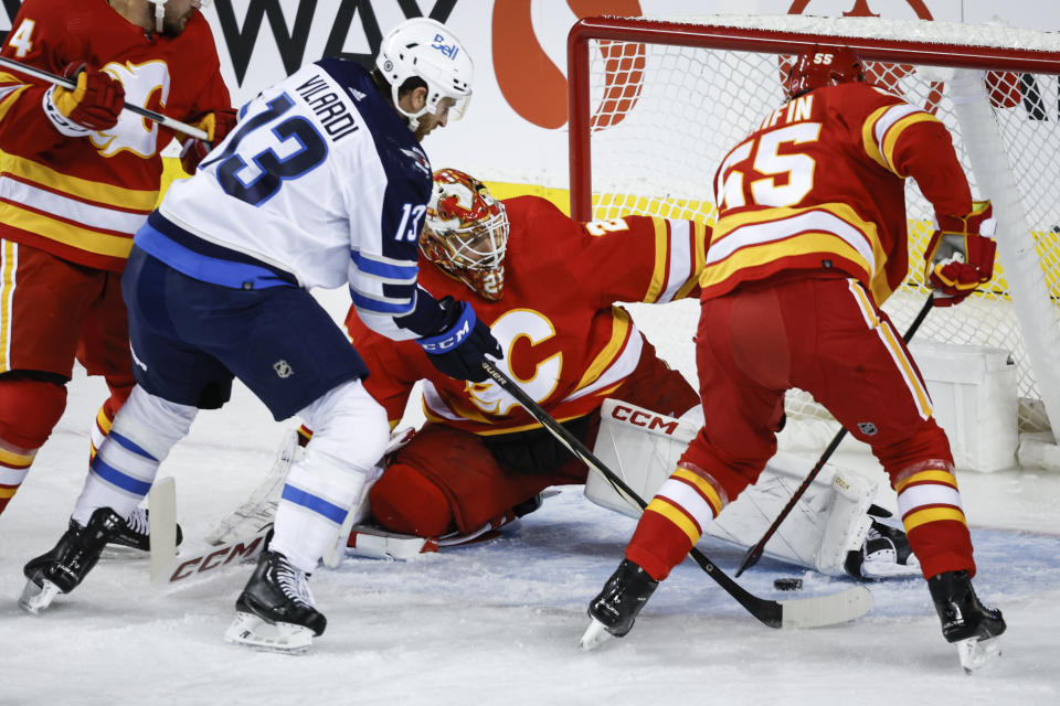 Winnipeg Jets forward Gabriel Vilardi (13) digs for the puck as Calgary Flames goalie Jacob Markstrom and defenseman Noah Hanifin try to clear it during the first period of an NHL hockey game Wednesday, Oct. 11, 2023, in Calgary, Alberta. (Jeff McIntosh/The Canadian Press via AP)
