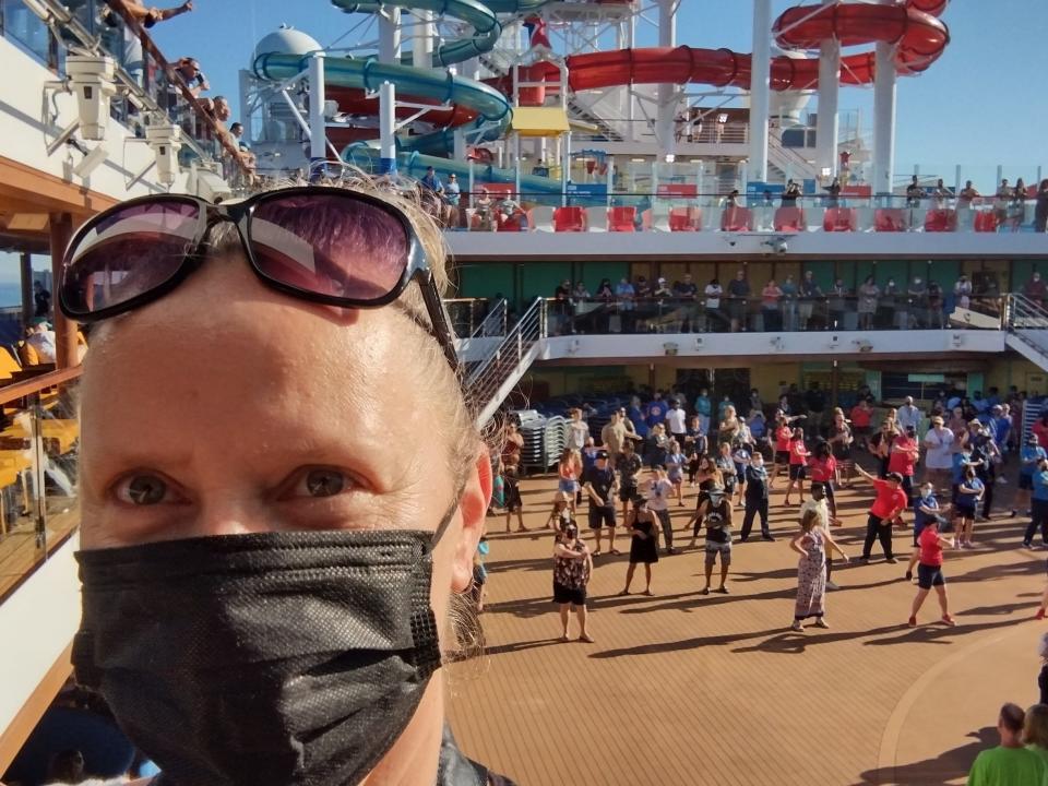 A woman wearing a face mask with sunglasses on her head taking a selfie on a cruise ship deck.