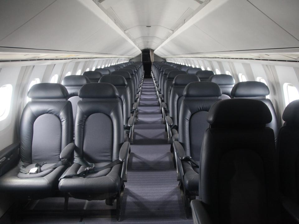 A view of an empty cabin inside a Concorde with rows of black leather chairs.