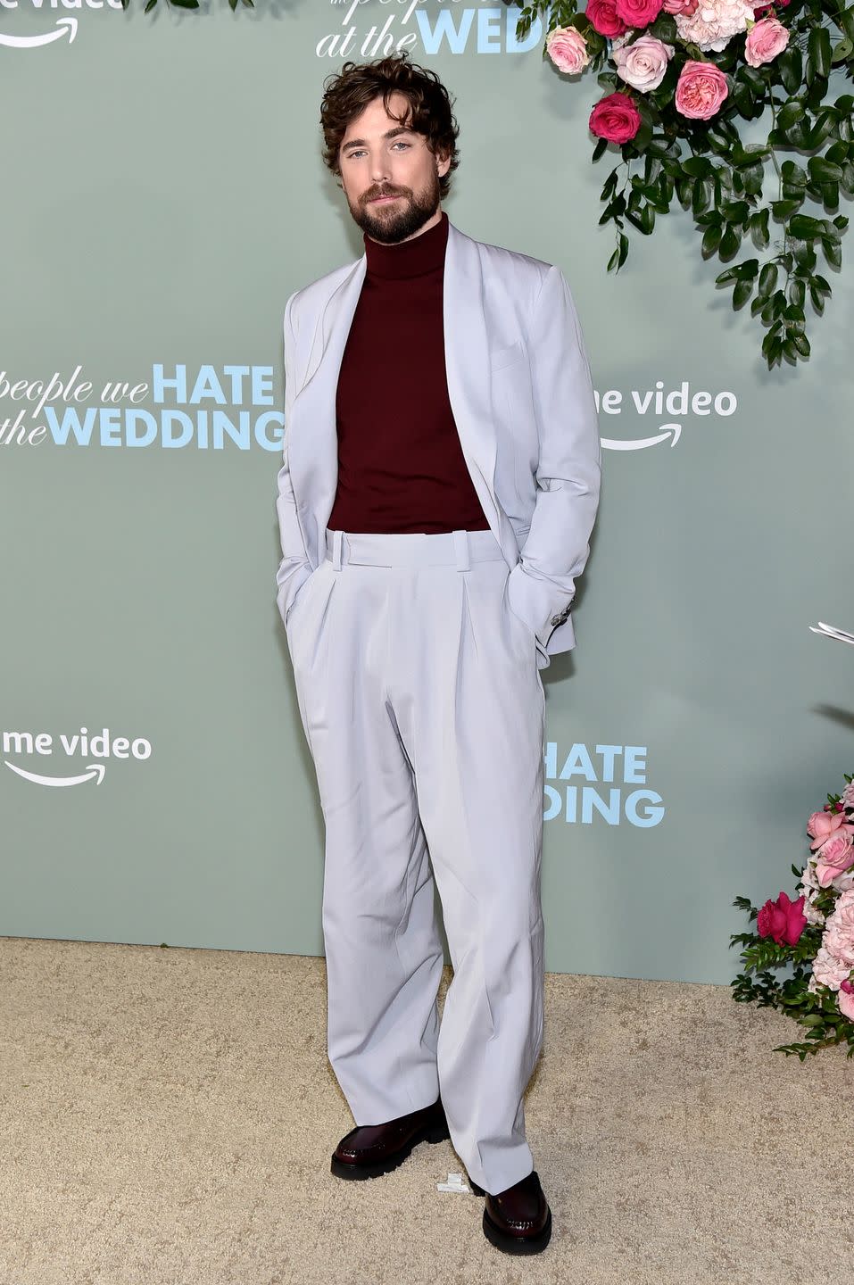 dustin milligan attends an event wearing a burgundy turtleneck and a pale grey suit