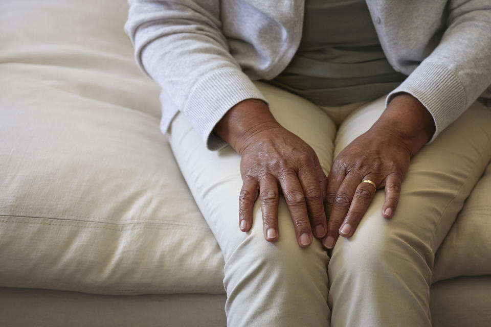 An older adult sitting on a couch, with their hands showing a wedding ring