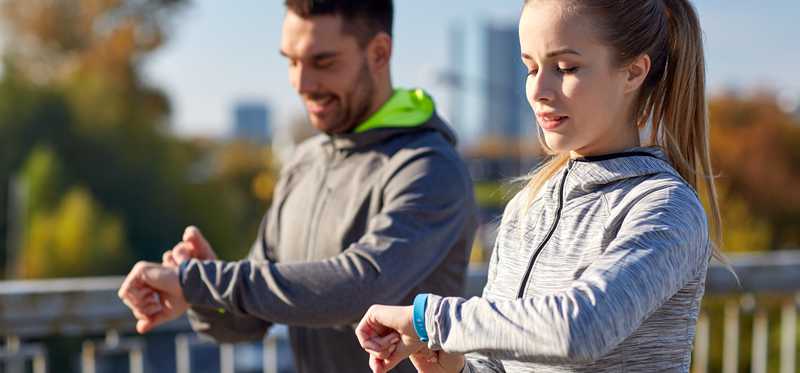 Two young people check their fitness trackers.