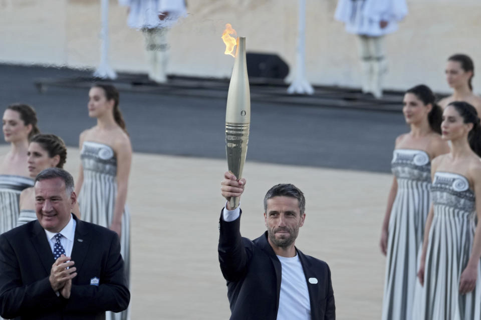 Tony Estanguet, President of Paris 2024, right, holds the Olympic flame while Spyros Capralos, head of Greece's Olympic Committee, left, applauds during the flame handover ceremony at Panathenaic stadium, where the first modern games were held in 1896, in Athens, Friday, April 26, 2024. On Saturday the flame will board the Belem, a French three-masted sailing ship, built in 1896, to be transported to France. (AP Photo/Petros Giannakouris)