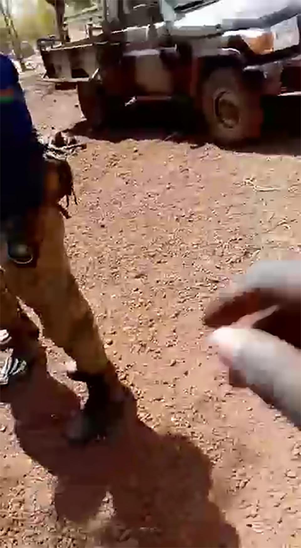 A soldier with the Burkina Faso flag on the shoulder of his shirt stands near the body of a dead child in a frame grab from a video that began circulating on social in the country in mid-February. The 83-second includes video shows the bodies of seven boys, including one whose head is seen being smashed in with a large rock. The military junta has denied its security forces were involved, but a frame-by-frame analysis by The Associated Press shows the killings happened inside a military base in the country’s north. (WhatsApp via AP)