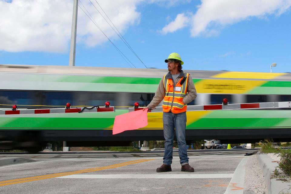 Palm Bay resident Sean Kearns holds a flag as a Brightline train passes by at 80 mph on Oct. 21 at the intersection of Southeast Walton Road near Savannas Preserve State Park in Port St. Lucie.