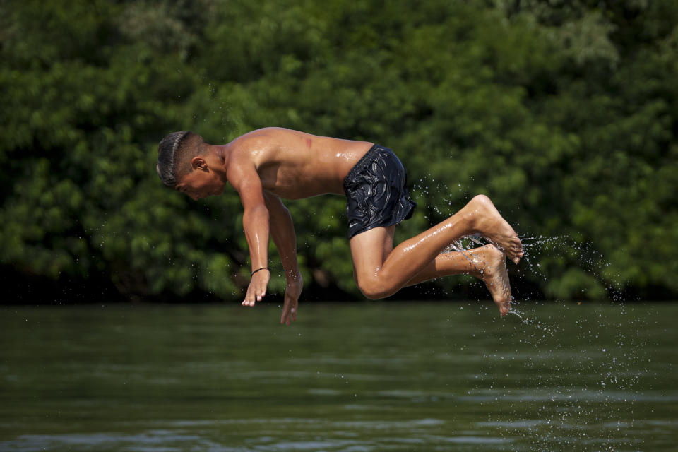 A boy jumps in the river Arges, outside Bucharest, Romania, Wednesday, July 12, 2023. Weather services issued a heat warning for the coming days in southern Romania, with temperatures expected to exceed 40 degrees Centigrade (104 Fahrenheit) in the shade. (AP Photo/Andreea Alexandru)