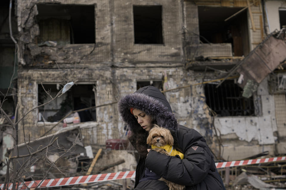 A woman holding a small dog walks in front of an apartment in a block which was destroyed by an artillery strike in Kyiv, Ukraine, Monday, March 14, 2022. Russia's military forces kept up their punishing campaign to capture Ukraine's capital with fighting and artillery fire in Kyiv's suburbs Monday after an airstrike on a military base near the Polish border brought the war dangerously close to NATO's doorstep.(AP Photo/Vadim Ghirda)