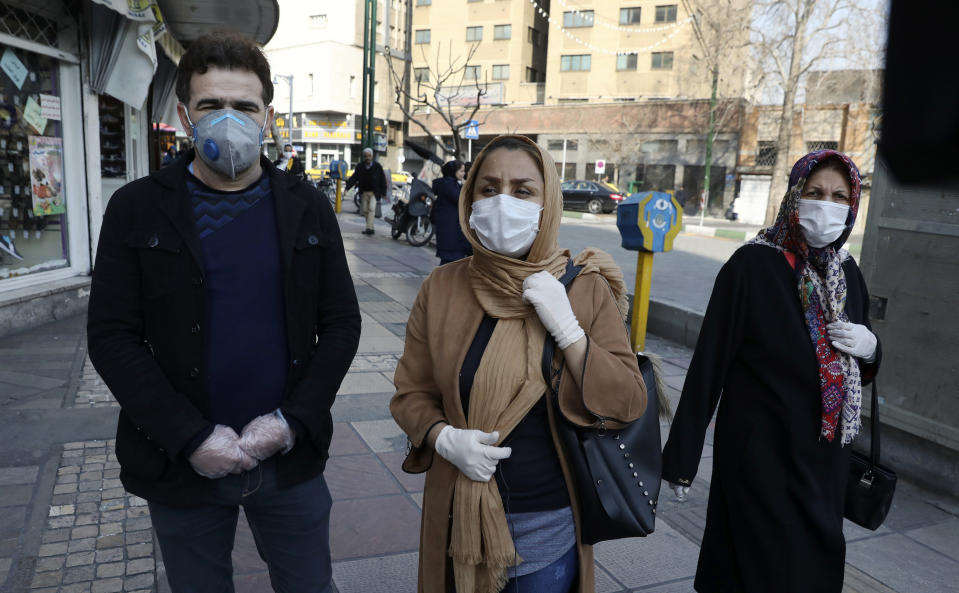 Tehran resident Leila Tayyeb, center, with her husband wearing mask and gloves, speaks with The Associated Press, as a woman walks past, in downtown Tehran, Iran, Thursday, Feb. 27, 2020. Amid fear and uncertainty caused by the spread of a new virus, Iranians are taking extra caution to avoid getting infected, as authorities canceled Friday prayers in Tehran, Qom and other cities. (AP Photo/Vahid Salemi)