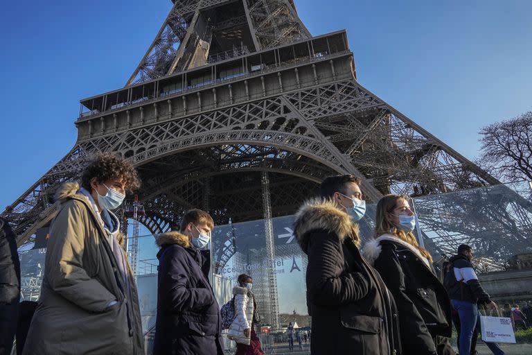 Personas con mascarillas para protegerse del Covid-19 caminan frente a la Torre Eiffel, el martes 21 de diciembre de 2021, en París