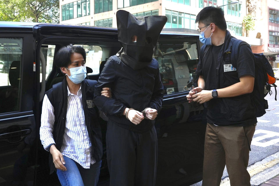 FILE - A hooded suspect is accompanied by police officers to search evidence at office in Hong Kong Thursday, July 22, 2021. Five Hong Kong speech therapists were convicted of sedition on Wednesday after they printed a series of children’s books about sheep and wolves that a court said was aimed at inciting hatred against authorities. (AP Photo/Vincent Yu)