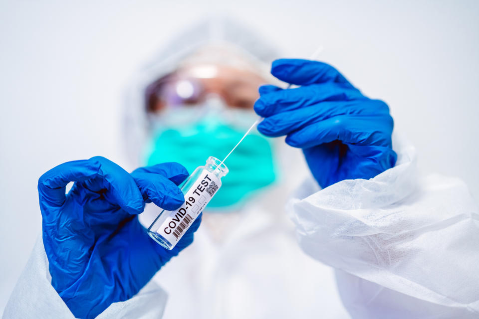 Doctor in protective gloves & workwear holding open test tube and taking out sampling swab for novel Covid-19 test in laboratory.