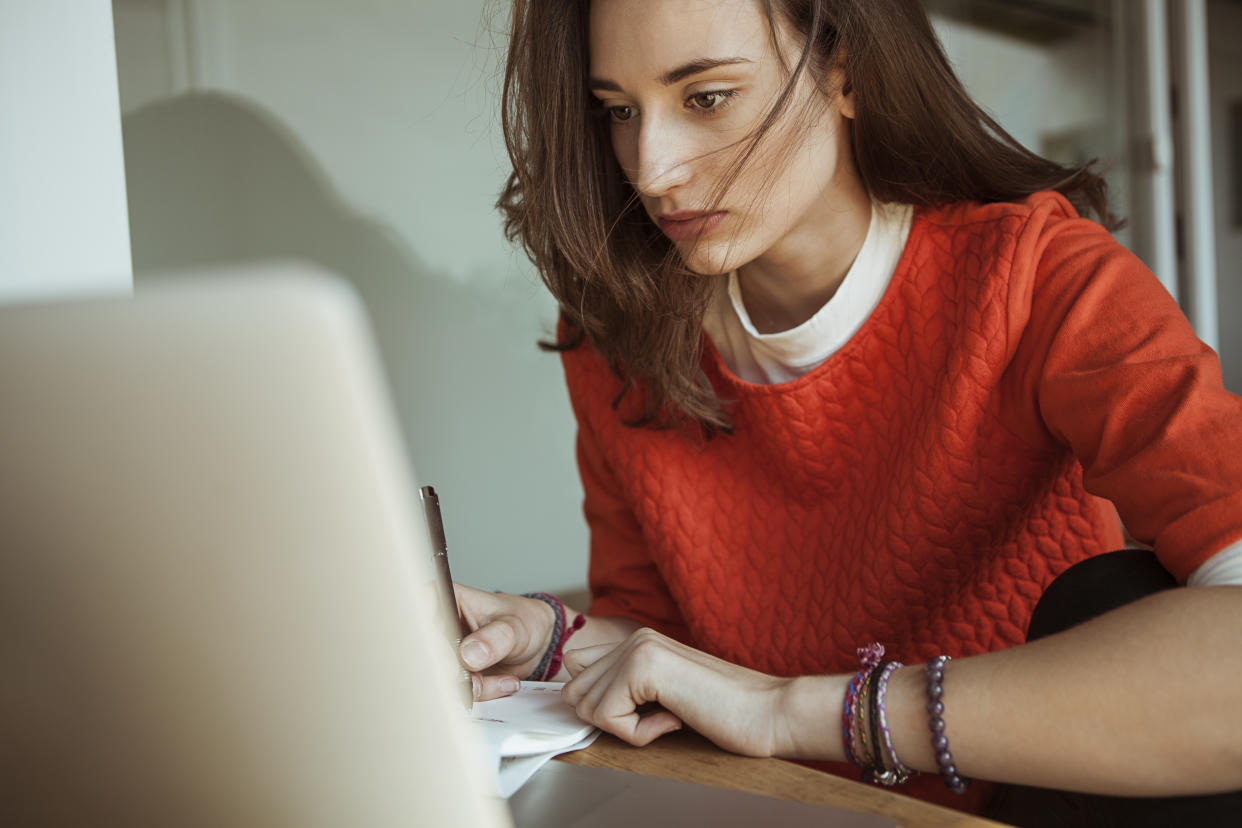 Young woman using laptop and taking notes