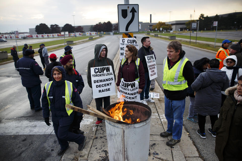 Canada Post workers stand around a barrel fire in Toronto during one of the first days of rotating strikes across Canada on Oct. 23, 2018. Photo from Getty Images.