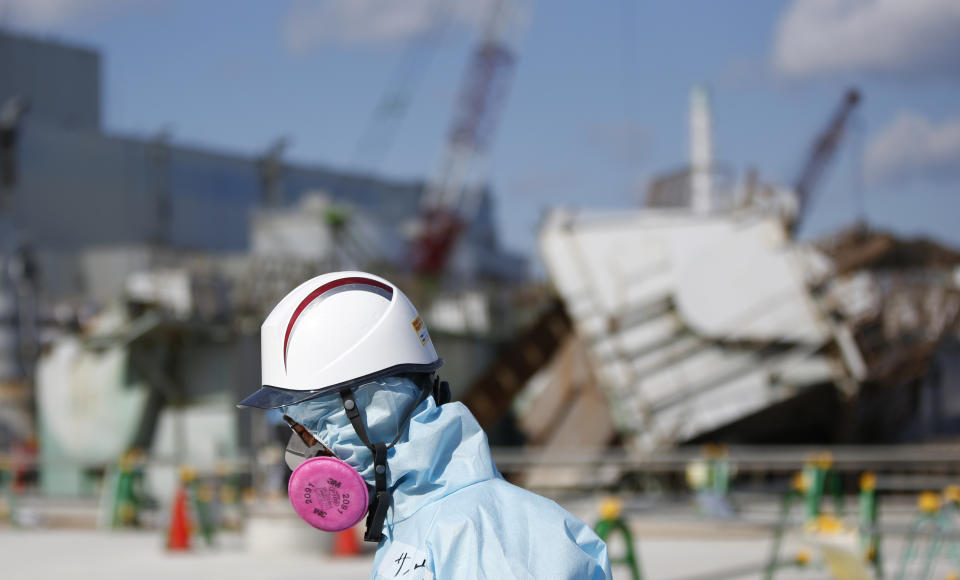 A Tokyo Electric Power Co. (TEPCO) employee, wearing a protective suit and a mask, walks in front of the No. 1 reactor building at TEPCO's tsunami-crippled Fukushima Daiichi nuclear power plant in Okuma town, Fukushima prefecture, Japan February 10, 2016.  REUTERS/Toru Hanai       TPX IMAGES OF THE DAY     