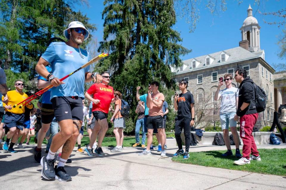 Paul Johnson is followed by a pack of runners and is cheered on by members of the Penn State club cross country team as he runs past Old Main on the Penn State University Park campus on Tuesday, April 16, 2024. Johnson, who is a Penn State alum, is running across the United States from Los Angeles to New York City while raising money for Team RWB.