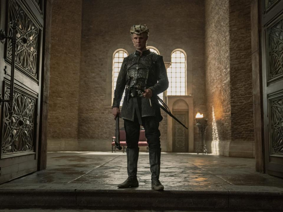 matt smith as daemon targaryen, standing in an open doorway with a sword and wearing a makeshift crown. his hair is cropped short